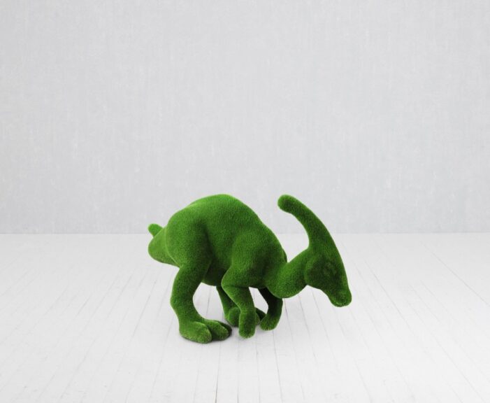 Green turf-covered dinosaur topiary sculpture photographed on a white floor.