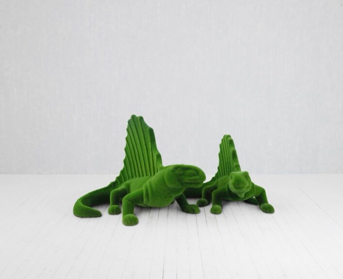 Two dinosaur-shaped topiary sculptures covered in artificial turf, shown on a white floor