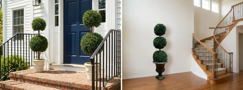 A pair of artificial double ball topiaries in white urns on the brick steps of a white house with a navy door, and a preserved triple ball topiary in a black urn in a front hall by a curved staircase.