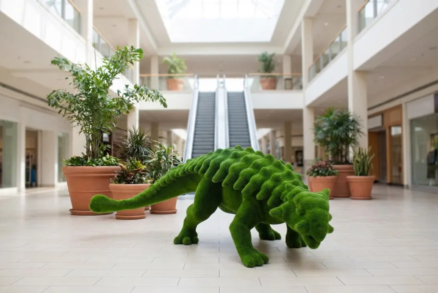 A large sail-backed dinosaur sculpture in artificial moss on the floor of a shopping center atrium