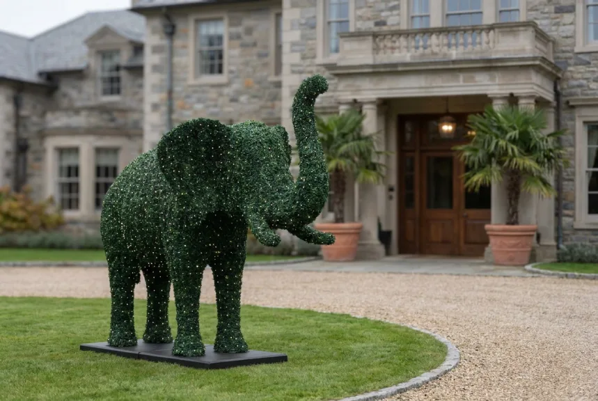 A life-size elephant in outdoor boxwood foliage on its base beside a hotel forecourt