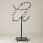 Monogram letter A topiary frame in Flowing script style, bare galvanized steel on an adjustable stand