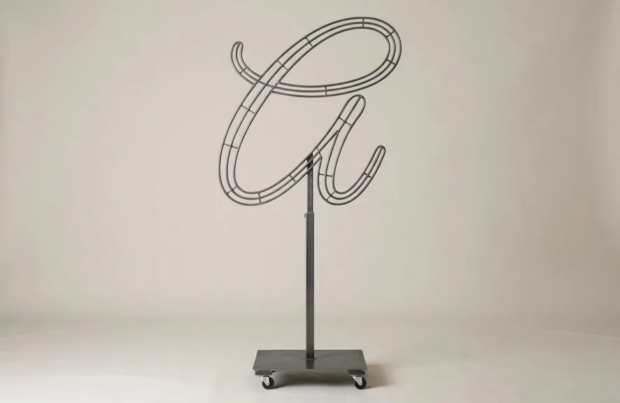 Monogram letter A topiary frame in Flowing script style, bare galvanized steel on an adjustable stand