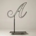 Monogram letter A topiary frame in Script style, bare galvanized steel on an adjustable stand