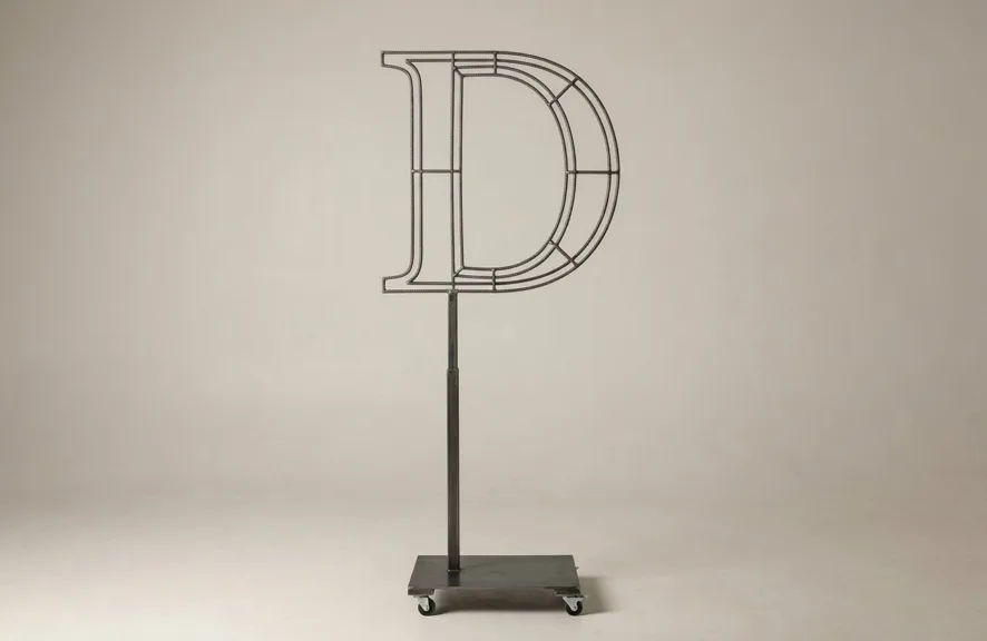 Monogram letter D topiary frame in Cinzel style, bare galvanized steel on an adjustable stand