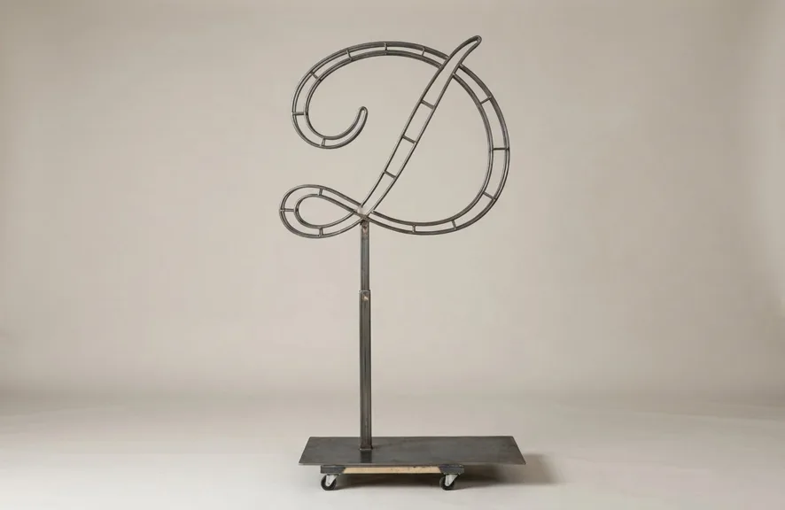 Monogram letter D topiary frame in Flowing script style, bare galvanized steel on an adjustable stand