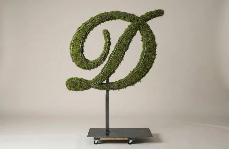 Monogram letter D topiary in Script style, packed with green moss, on an adjustable stand