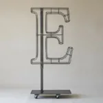 Monogram letter E topiary frame in Cinzel style, bare galvanized steel on an adjustable stand