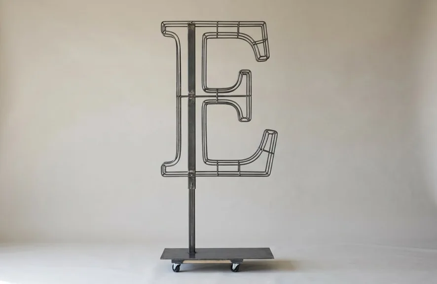 Monogram letter E topiary frame in Cinzel style, bare galvanized steel on an adjustable stand