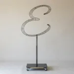 Monogram letter E topiary frame in Flowing script style, bare galvanized steel on an adjustable stand