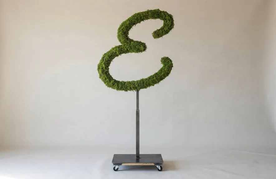Monogram letter E topiary in Flowing script style, packed with green moss, on an adjustable stand