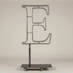 Monogram letter E topiary frame in Roman style, bare galvanized steel on an adjustable stand