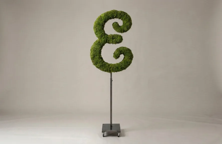 Monogram letter E topiary in Script style, packed with green moss, on an adjustable stand
