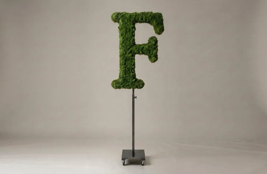 Monogram letter F topiary in Roman style, packed with green moss, on an adjustable stand