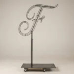 Monogram letter F topiary frame in Script style, bare galvanized steel on an adjustable stand