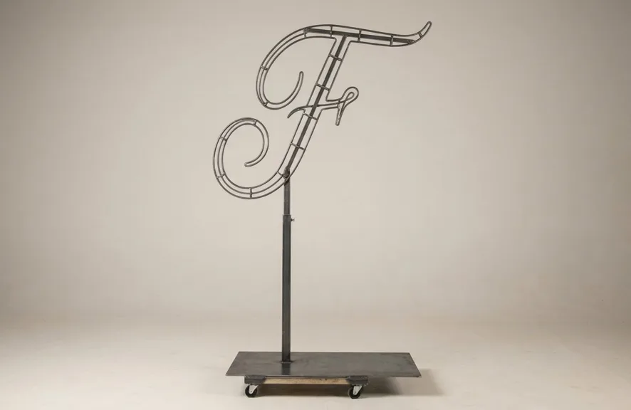 Monogram letter F topiary frame in Script style, bare galvanized steel on an adjustable stand