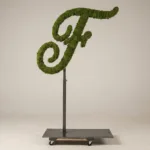 Monogram letter F topiary in Script style, packed with green moss, on an adjustable stand