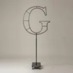 Monogram letter G topiary frame in Cinzel style, bare galvanized steel on an adjustable stand
