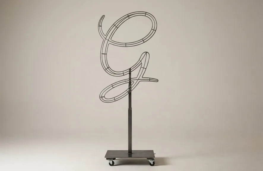 Monogram letter G topiary frame in Flowing script style, bare galvanized steel on an adjustable stand
