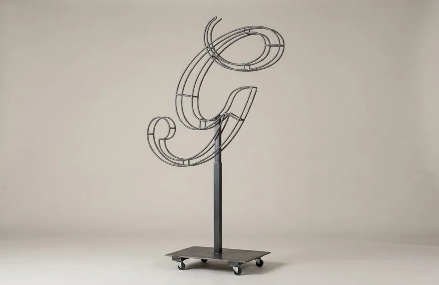 Monogram letter G topiary frame in Script style, bare galvanized steel on an adjustable stand