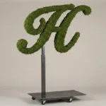 Monogram letter H topiary in Script style, packed with green moss, on an adjustable stand