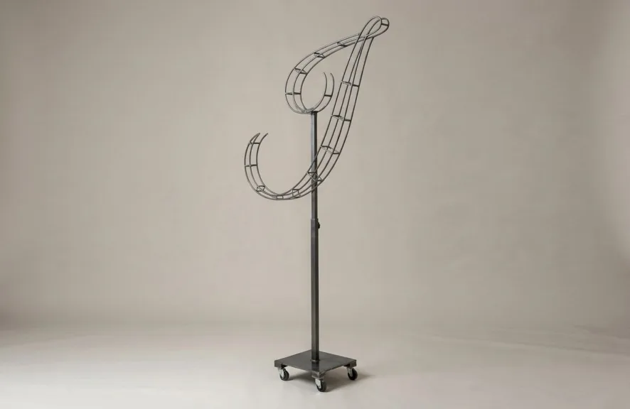 Monogram letter J topiary frame in Flowing script style, bare galvanized steel on an adjustable stand