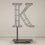 Monogram letter K topiary frame in Cinzel style, bare galvanized steel on an adjustable stand