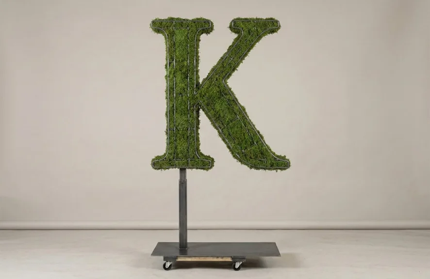 Monogram letter K topiary in Cinzel style, packed with green moss, on an adjustable stand