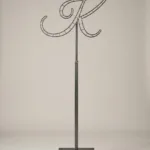 Monogram letter K topiary frame in Flowing script style, bare galvanized steel on an adjustable stand