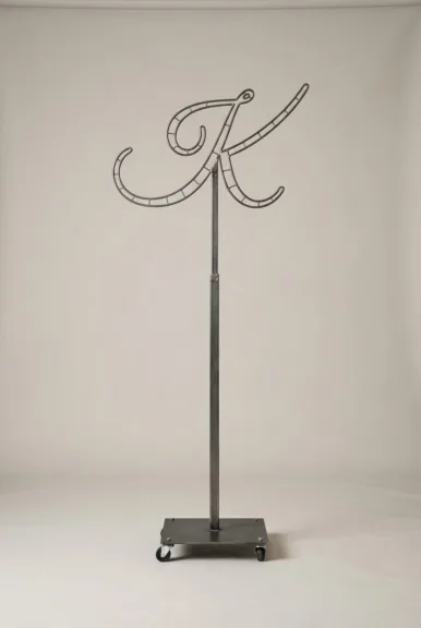 Monogram letter K topiary frame in Flowing script style, bare galvanized steel on an adjustable stand