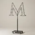 Monogram letter M topiary frame in Cinzel style, bare galvanized steel on an adjustable stand