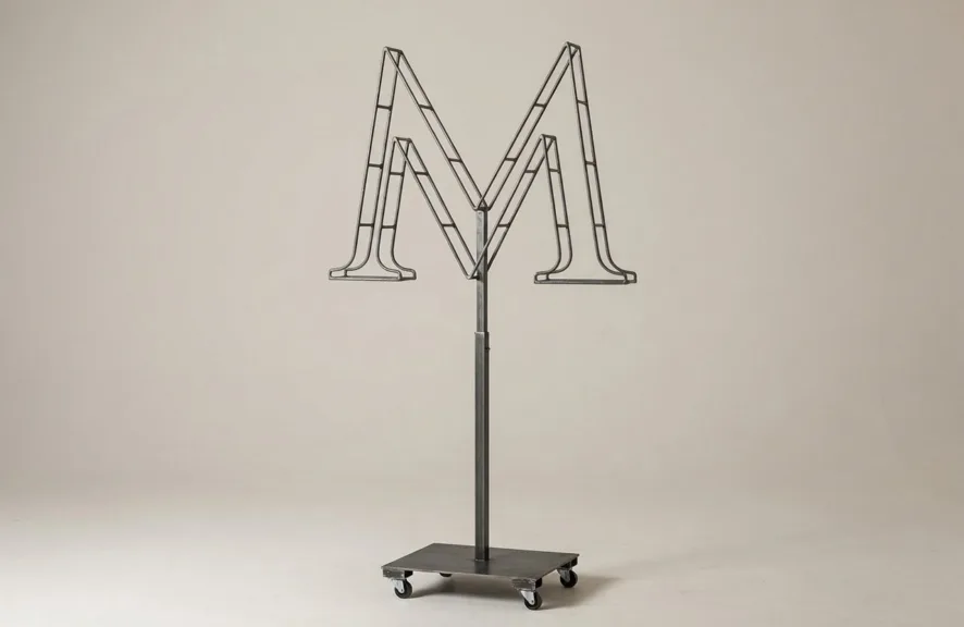 Monogram letter M topiary frame in Cinzel style, bare galvanized steel on an adjustable stand