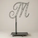 Monogram letter M topiary frame in Flowing script style, bare galvanized steel on an adjustable stand