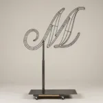 Monogram letter M topiary frame in Script style, bare galvanized steel on an adjustable stand