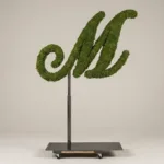 Monogram letter M topiary in Script style, packed with green moss, on an adjustable stand