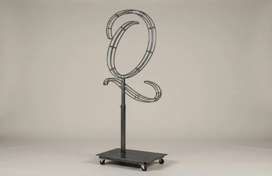 Monogram letter Q topiary frame in Flowing script style, bare galvanized steel on an adjustable stand