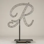 Monogram letter R topiary frame in Flowing script style, bare galvanized steel on an adjustable stand