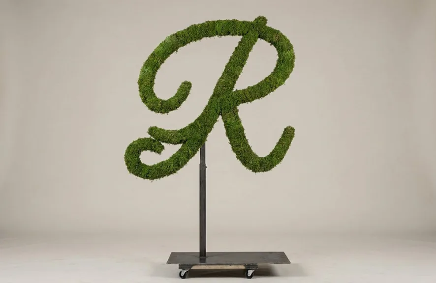 Monogram letter R topiary in Flowing script style, packed with green moss, on an adjustable stand