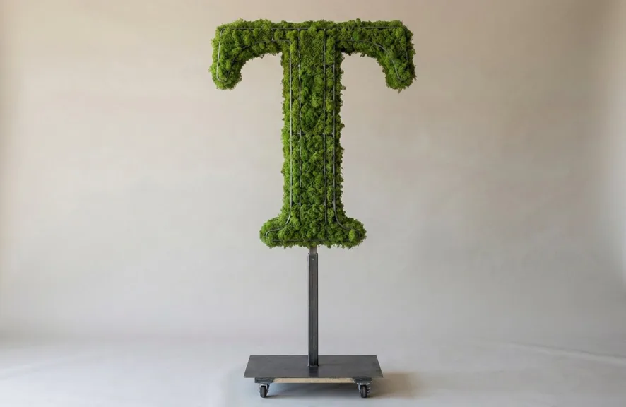 Monogram letter T topiary in Cinzel style, packed with green moss, on an adjustable stand