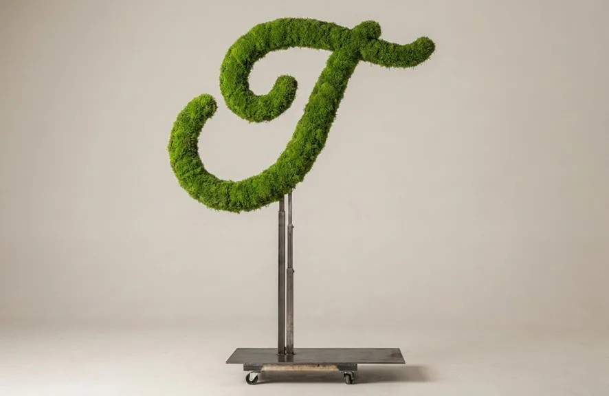 Monogram letter T topiary in Flowing script style, packed with green moss, on an adjustable stand