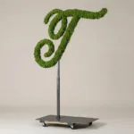 Monogram letter T topiary in Script style, packed with green moss, on an adjustable stand