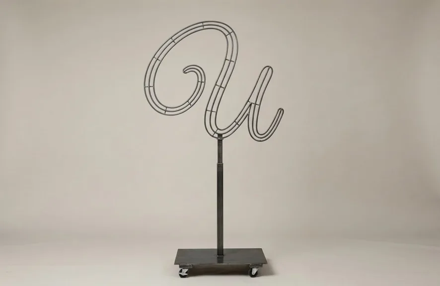 Monogram letter U topiary frame in Flowing script style, bare galvanized steel on an adjustable stand