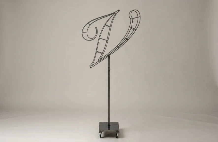 Monogram letter V topiary frame in Script style, bare galvanized steel on an adjustable stand