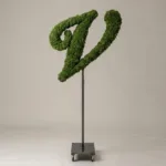 Monogram letter V topiary in Script style, packed with green moss, on an adjustable stand