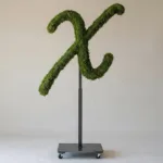 Monogram letter X topiary in Flowing script style, packed with green moss, on an adjustable stand