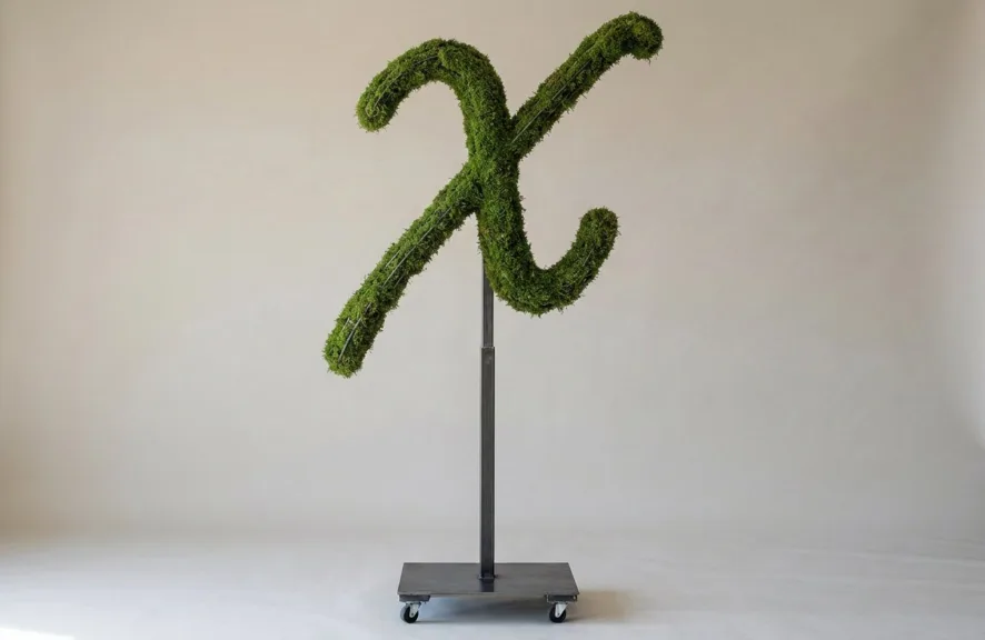 Monogram letter X topiary in Flowing script style, packed with green moss, on an adjustable stand