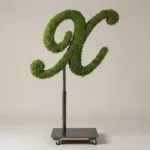 Monogram letter X topiary in Script style, packed with green moss, on an adjustable stand