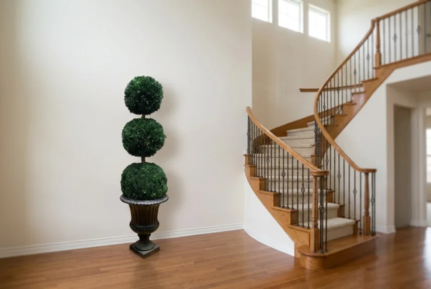 A preserved triple ball topiary in a dark urn beside a curved foyer staircase