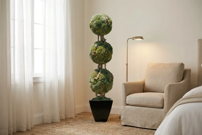 A moss ball topiary in a black planter beside a linen armchair in a reading nook