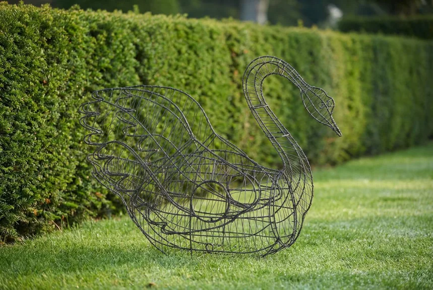 A bare black wire swan frame on a stone terrace beside clipped boxwood balls